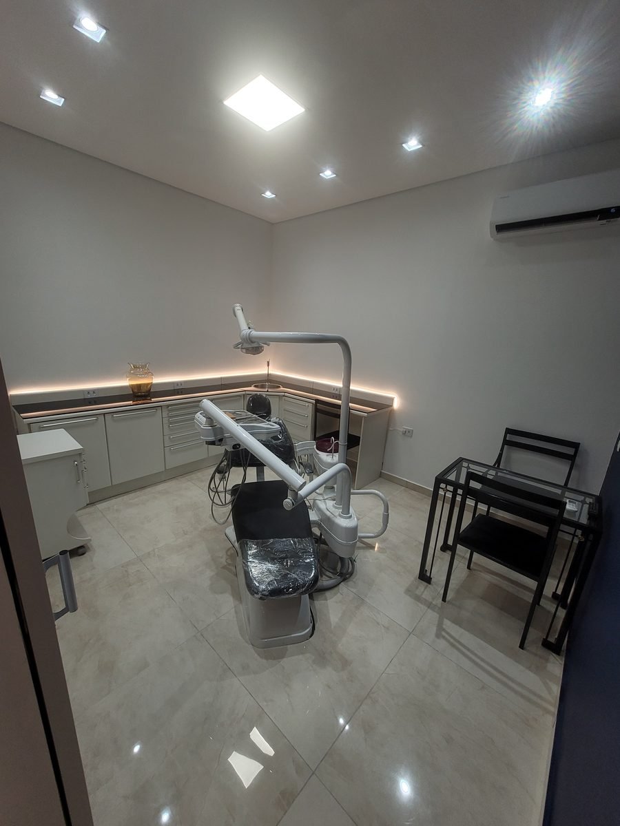Consultório com cadeira odontológica, armários brancos e luz indireta