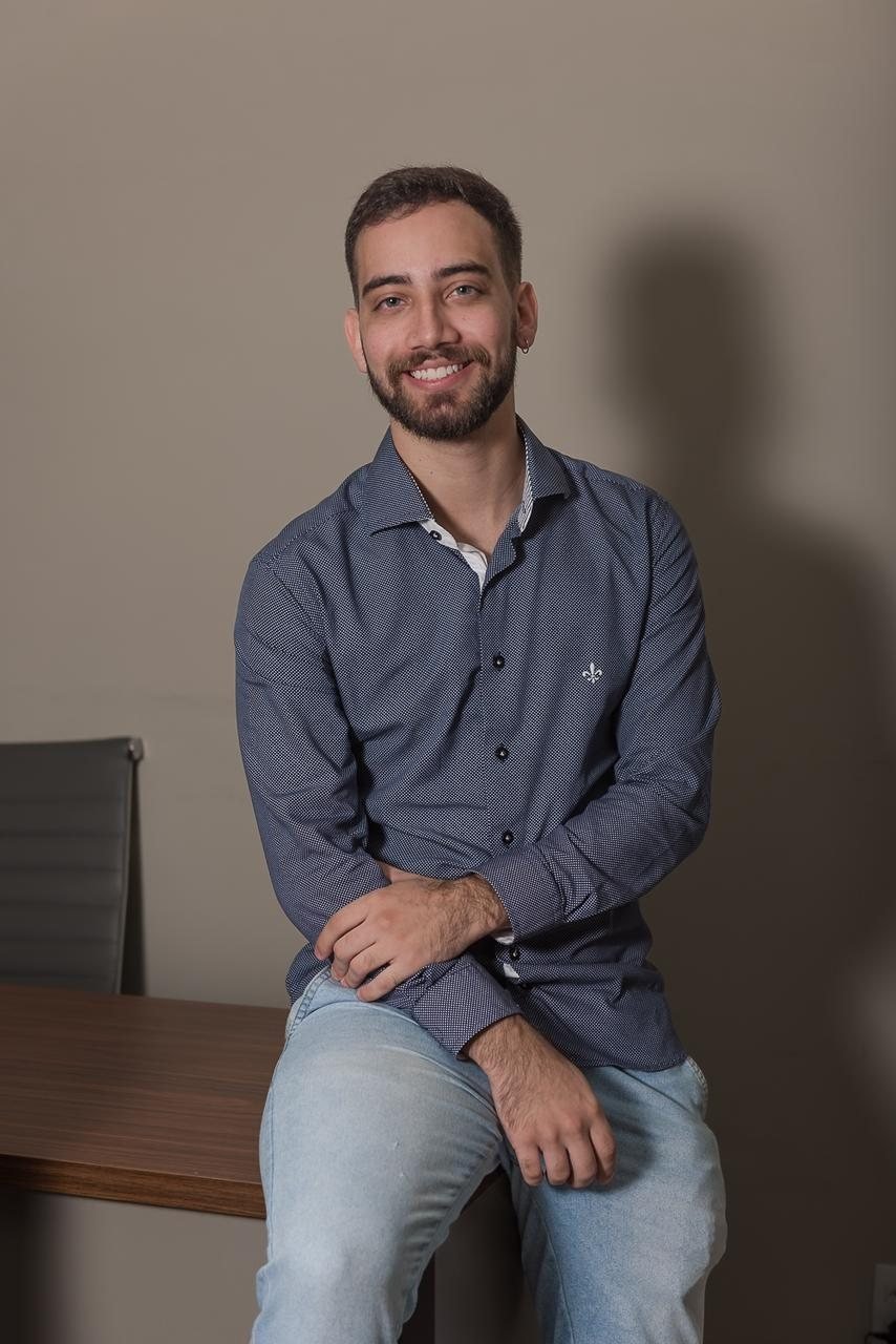 Dr. Gustavo Trindade sorrindo, sentado na mesa do consultório