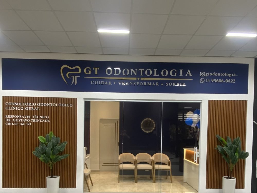 Fachada da GT Odontologia: placa azul com o logo dourado, paredes de madeira e porta de vidro