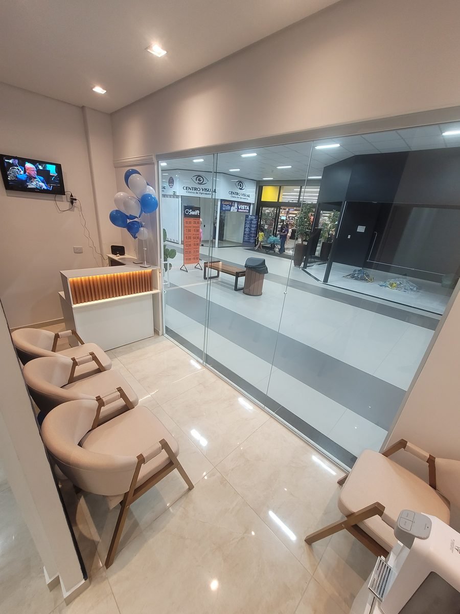Recepção da clínica, com poltronas claras, balcão de madeira e TV